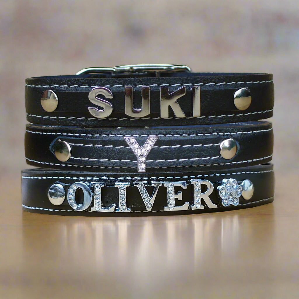 Black custom leather dog collars with sparkling rhinestone letters and charms, adding a touch of style and personalization.