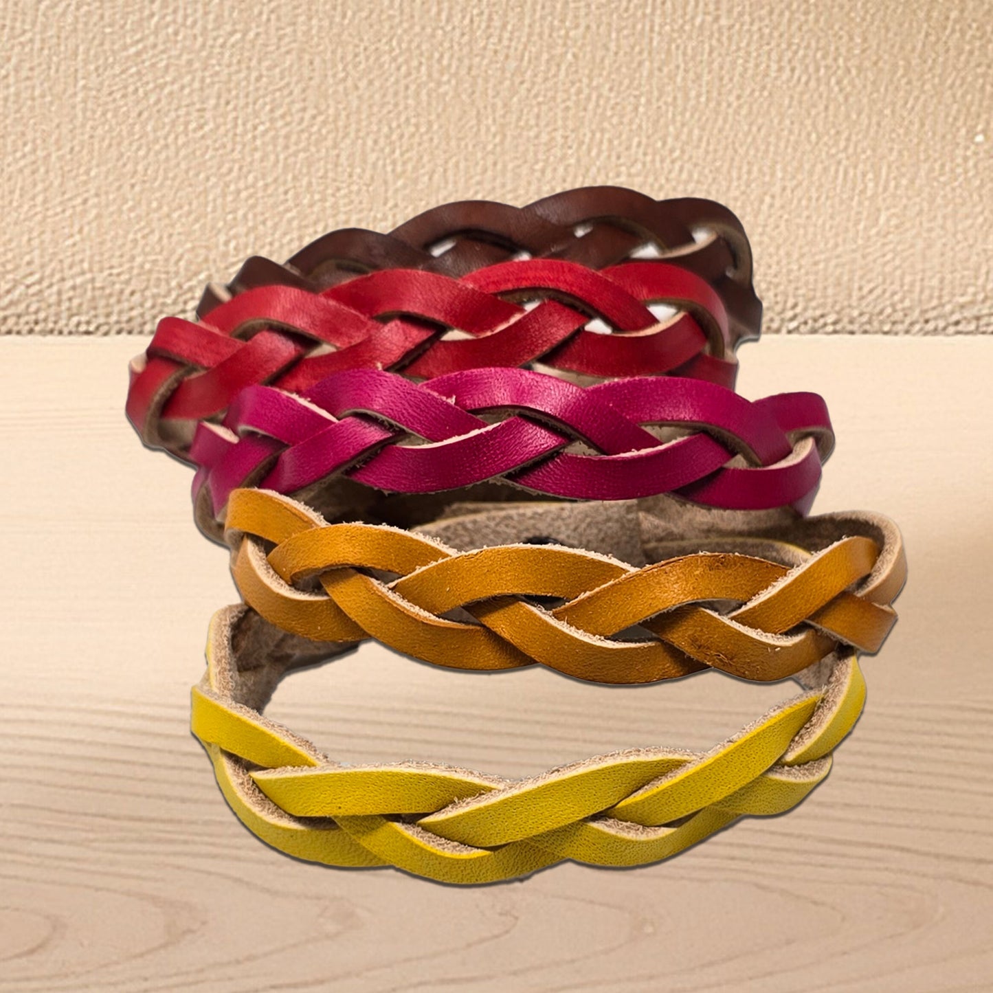 Braided leather bracelets in red, pink, tan, dark brown and yellow on a beige surface. Handmade braided leather bracelet crafted from vegetable tanned cowhide.