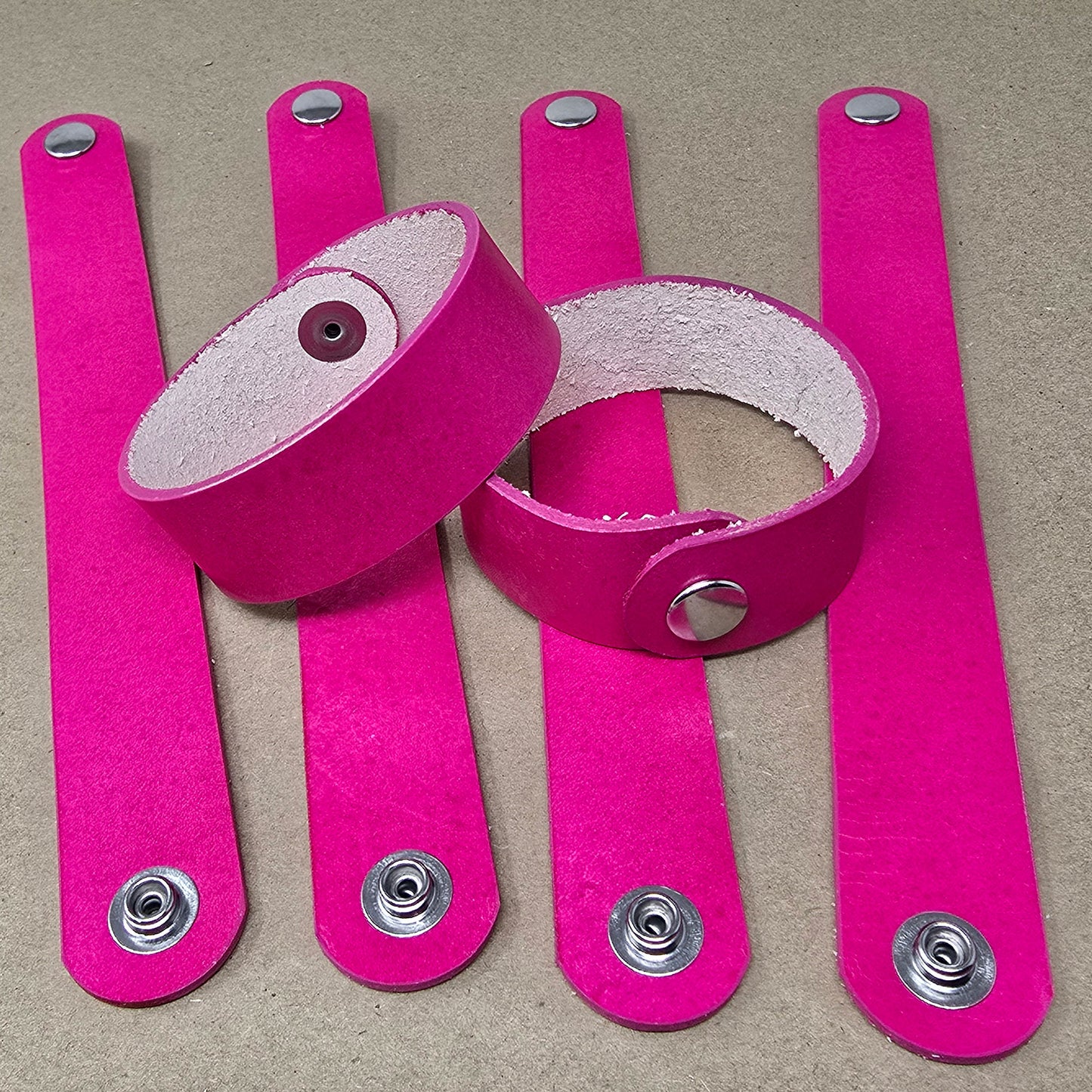 Flat lay of natural hot pink leather bracelets blank prepared for stamping, tooling, and carving in a DIY workshop setting